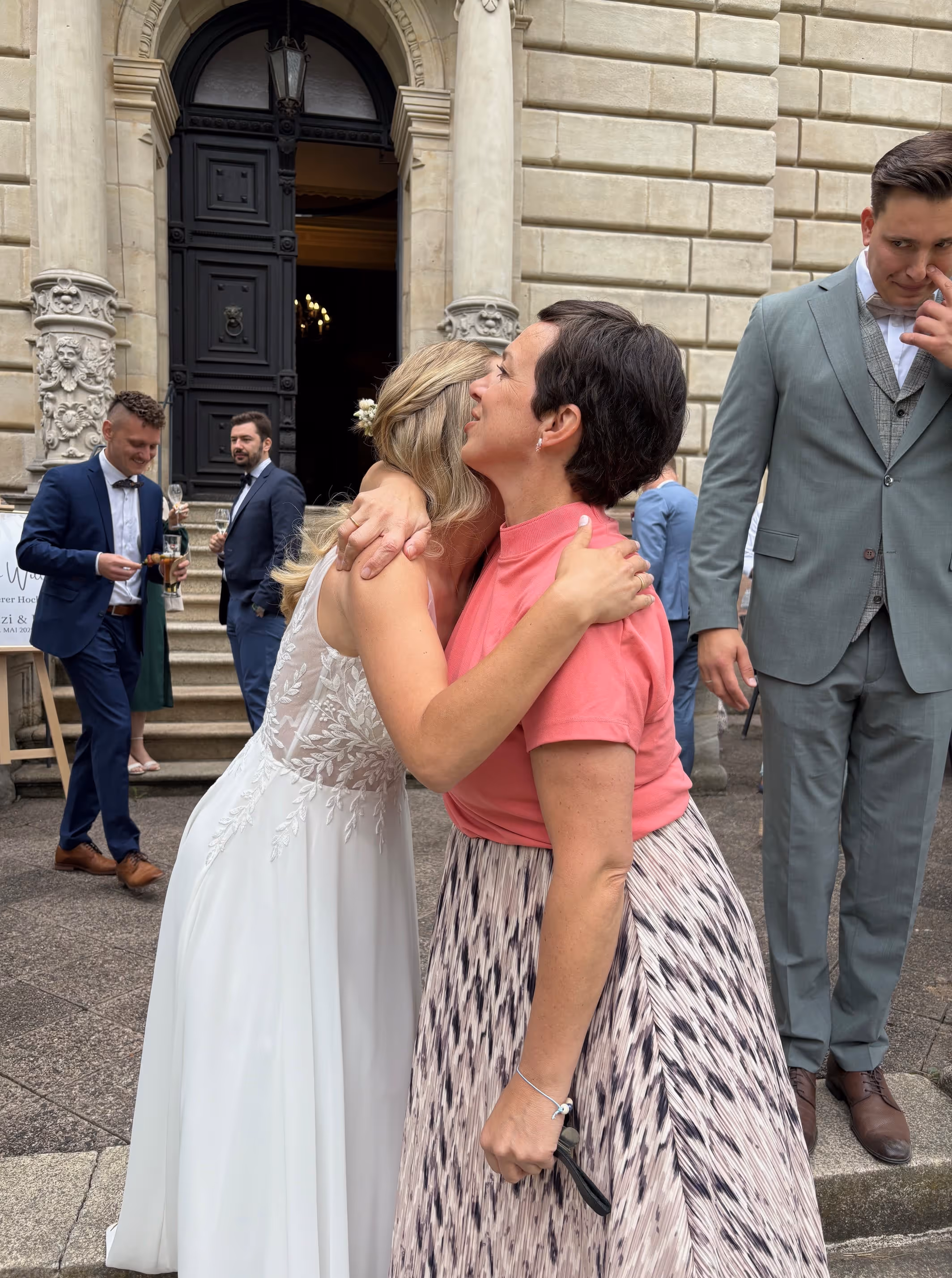 Braut umarmt Anna Fasciani - freie Traurednerin -  in pinkem Oberteil und gemustertem Rock vor einem historischen Gebäude bei einer Hochzeit.