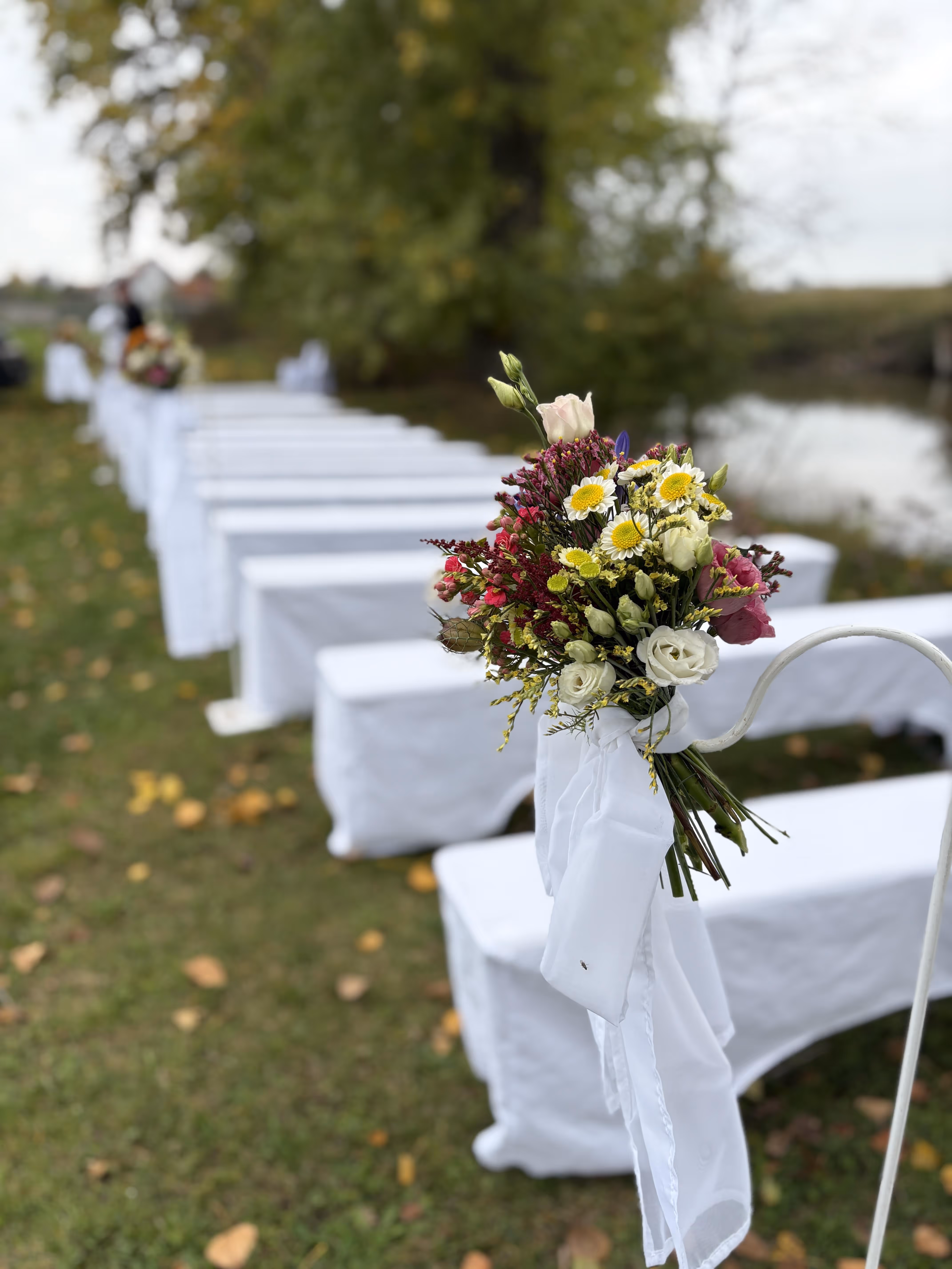 Blumenstrauß mit weißen, gelben und pinken Blüten an einer weißen Bank bei einer freien Trauung im Freien.