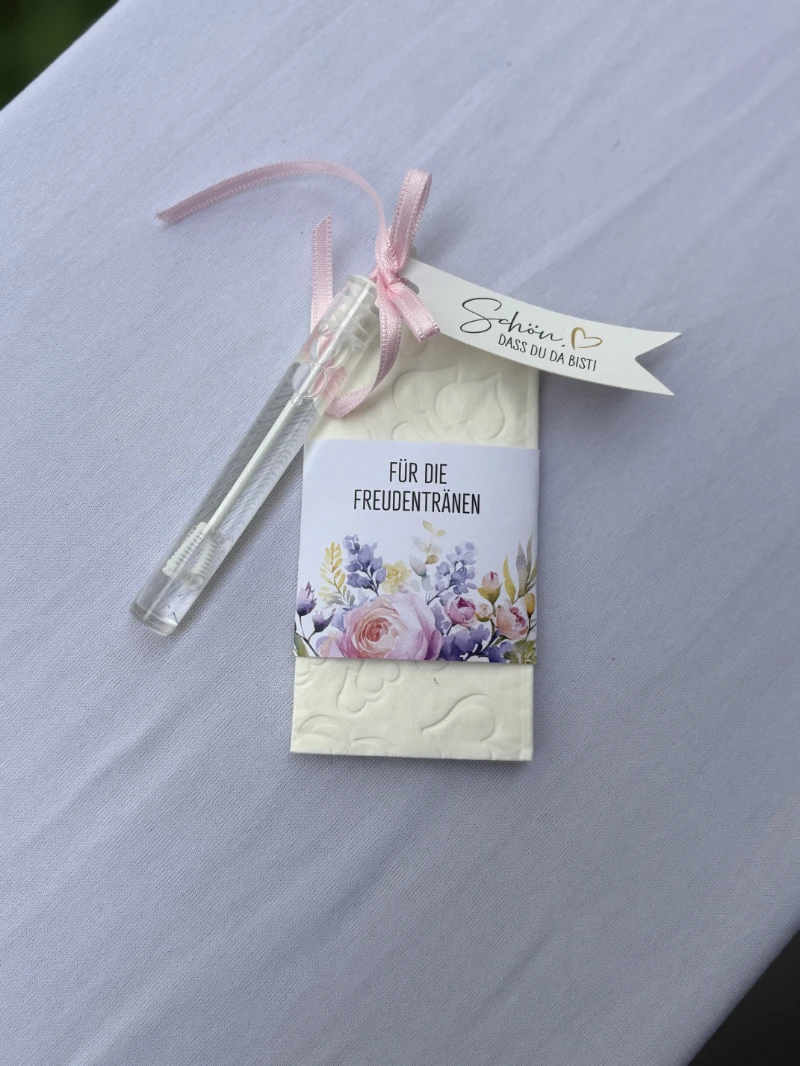 Seifenpapier mit Blumenmuster und Etikett "Für die Freudentränen" mit angehängter Seifenblasenflasche und Schleife auf weißer Stoffoberfläche.