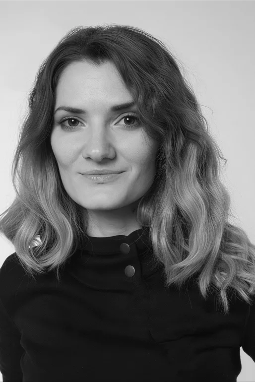 Portrait of a woman with wavy hair wearing a dark top against a plain background.