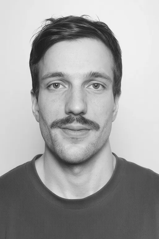 Black and white portrait of a man with a mustache wearing a plain shirt, looking directly at the camera.