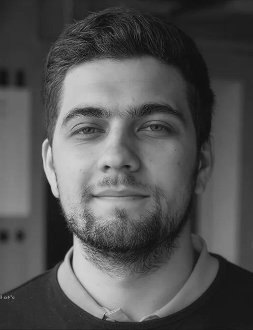 Black and white close-up portrait of a young man with short hair and a beard, looking directly at the camera with a neutral expression.