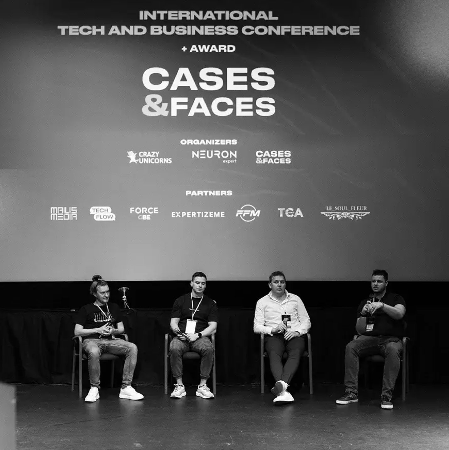 Portrait of a smiling young man with short hair wearing a black shirt with the word 'buśka' printed on it.