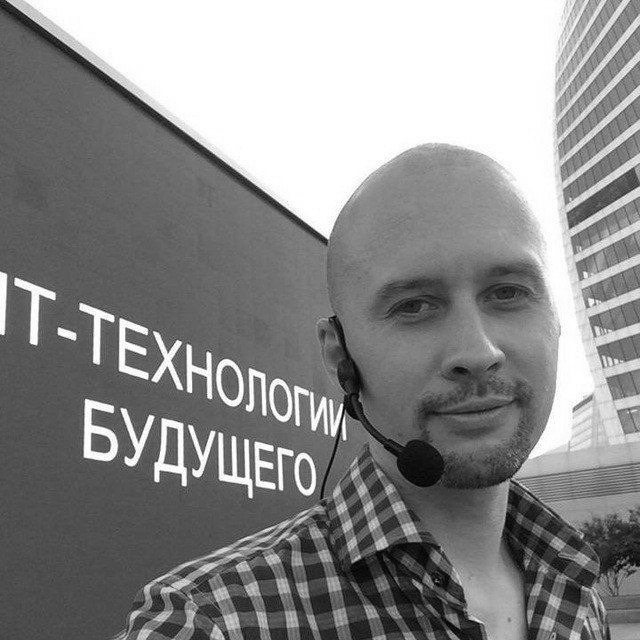 Black and white close-up portrait of a young man with short hair and a beard, looking directly at the camera with a neutral expression.