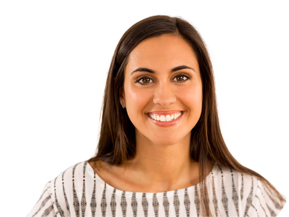 Smiling young woman with long brown hair wearing a white patterned top.