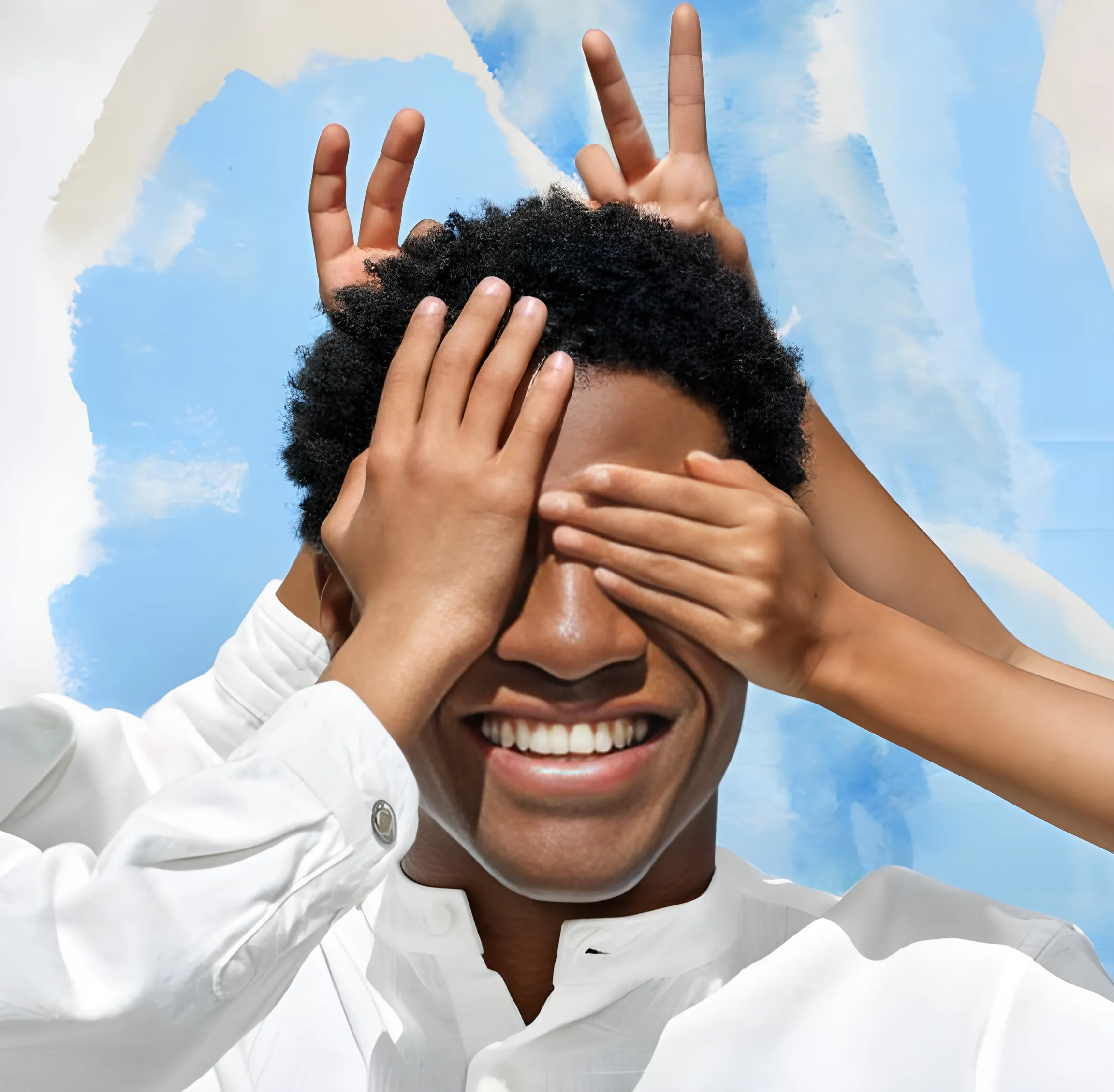 Un homme souriant portant une chemise blanche avec deux mains couvrant ses yeux et une autre montrant un signe de paix derrière sa tête.
