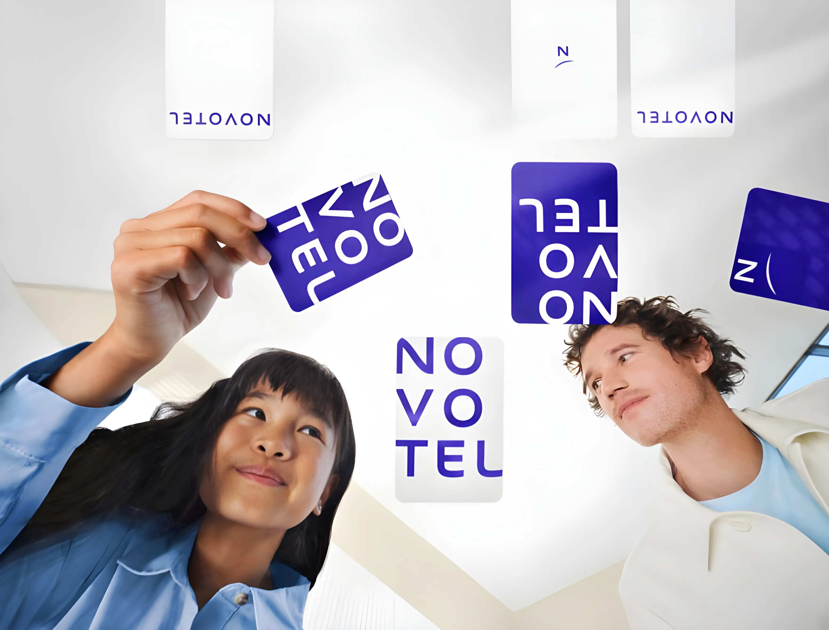 Deux jeunes adultes regardant et tenant des cartes blanches et bleues avec le texte "NOVOTEL" écrit dessus.