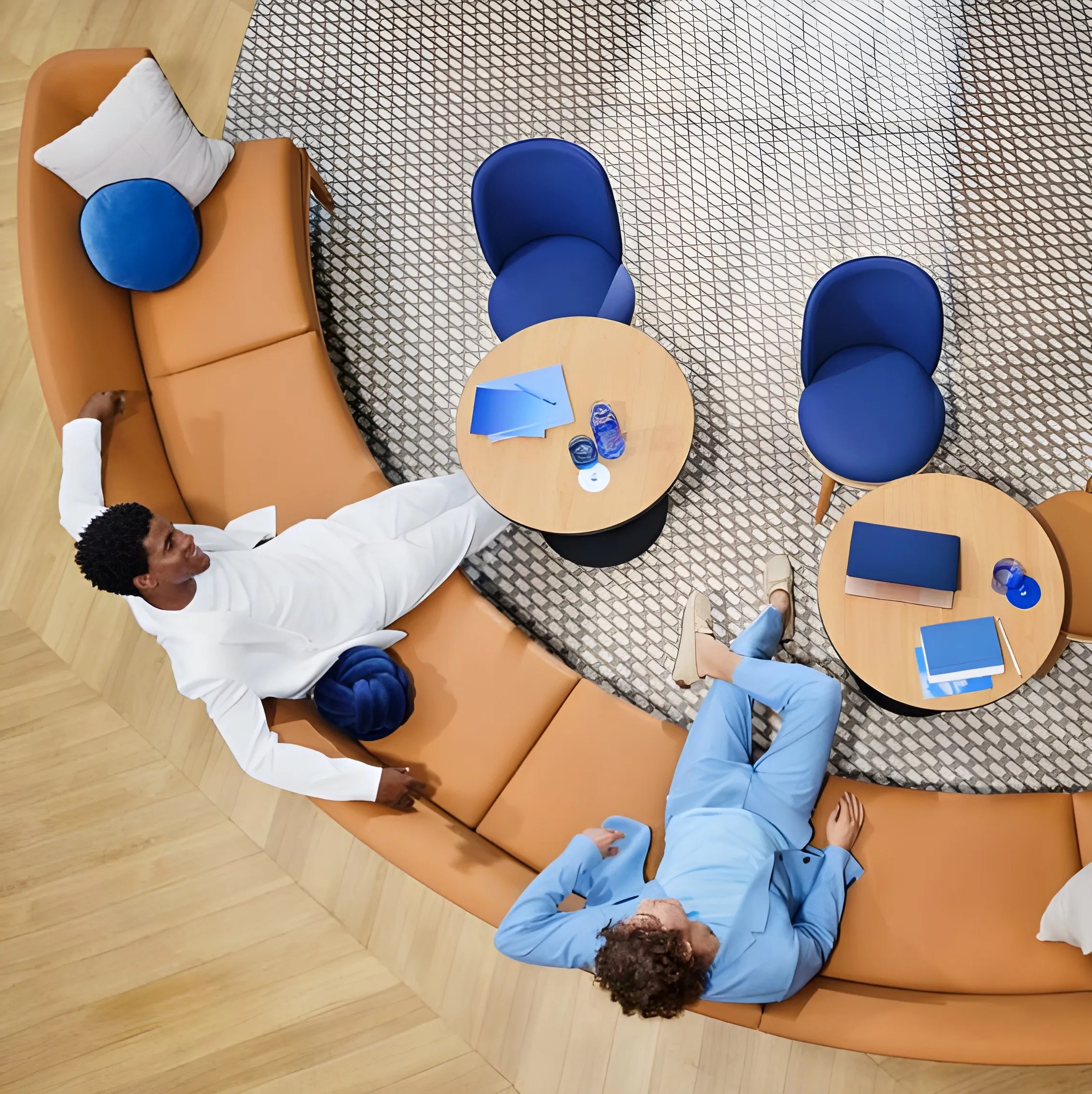 Deux personnes assises dans un canapé en cuir incurvé avec des tables rondes et des chaises bleues à l'intérieur d'un espace moderne.