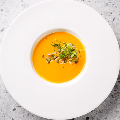 Cremige Suppe mit Samen und grünen Sprossen auf einem weißen Teller.