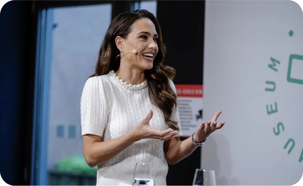 Franca Lehfeldt spricht auf einer Bühne während eines Vortrags, trägt ein weißes Kleid und gestikuliert mit einem Lächeln – Auftritt im Rahmen eines Events - mehr unter LEHFELDT& Stage.