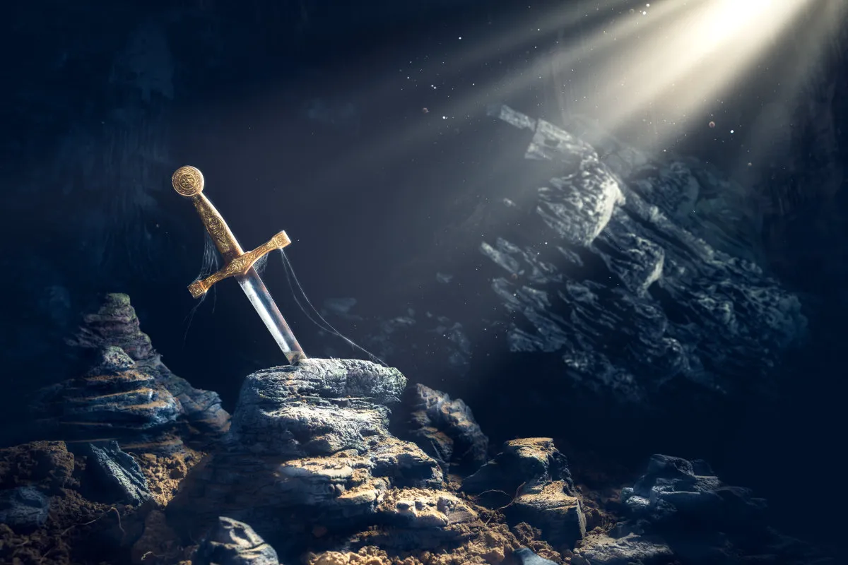 Ein in einen Felsen gestecktes, golden verziertes Schwert, beleuchtet von einem Lichtstrahl in einer dunklen, felsigen Umgebung.