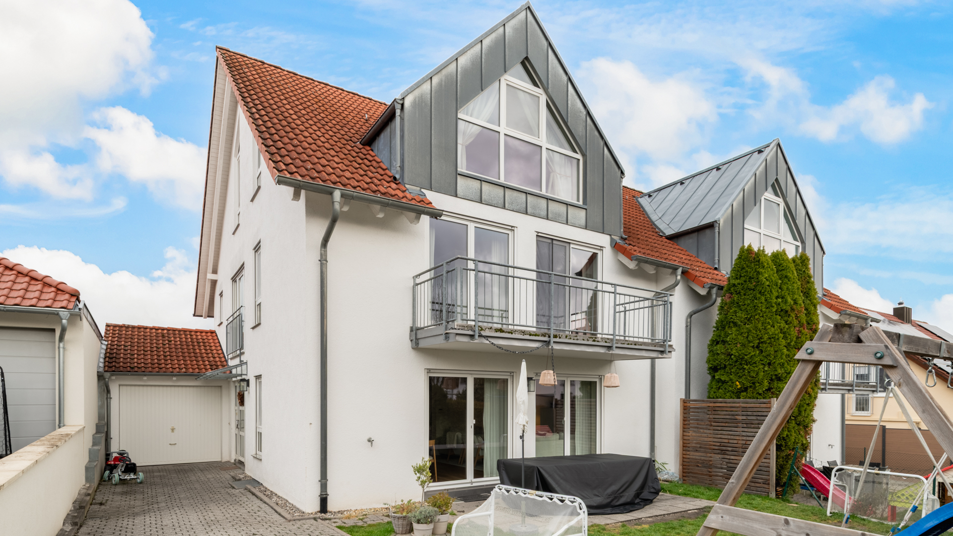 Weißes Haus mit rotem Dach und großer Dachgaupe mit langer Hofeinfahrt und Garage