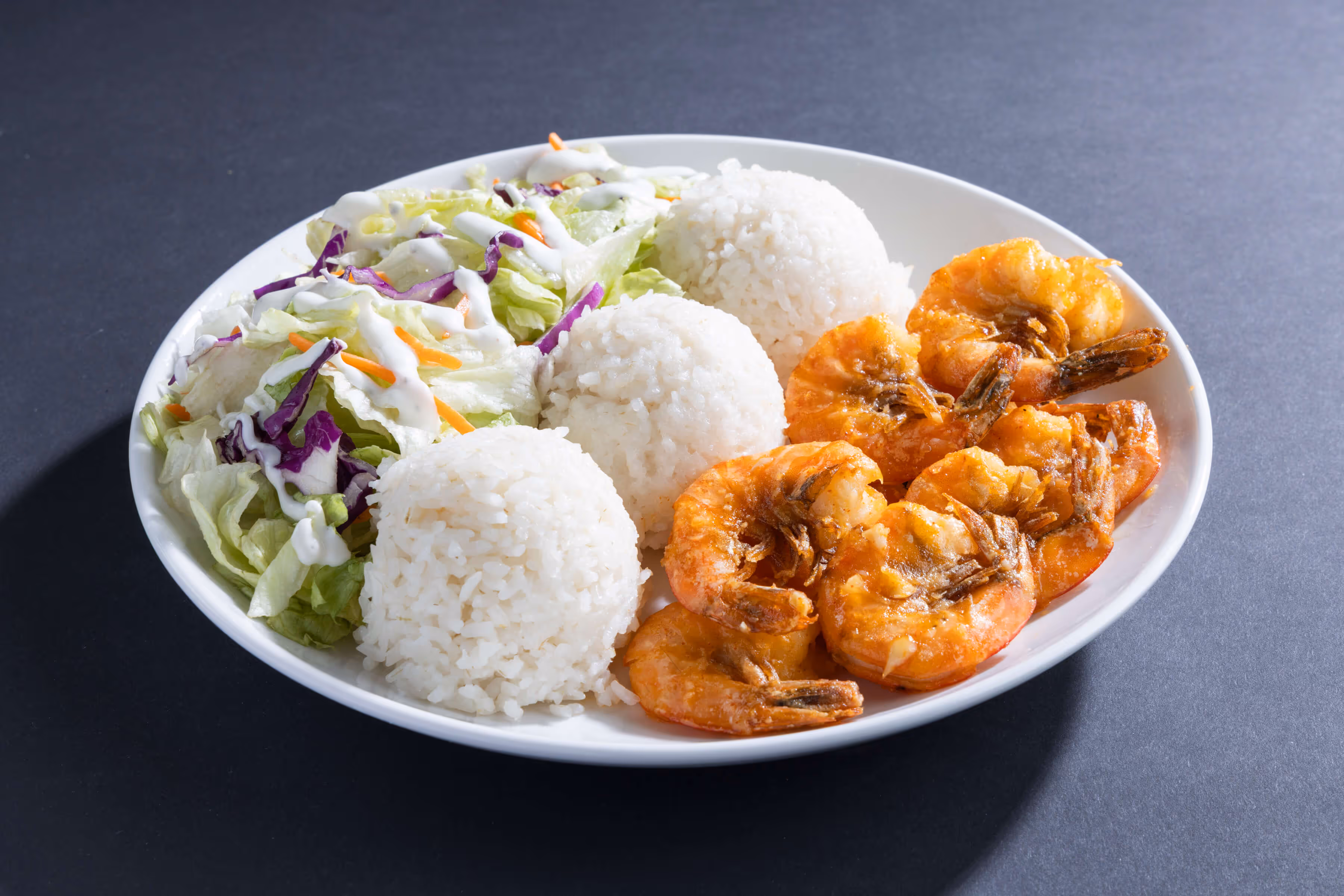 Plate with garlic butter shrimp, three servings of white rice, and salad with lettuce, purple cabbage, carrots, and ranch dressing.
