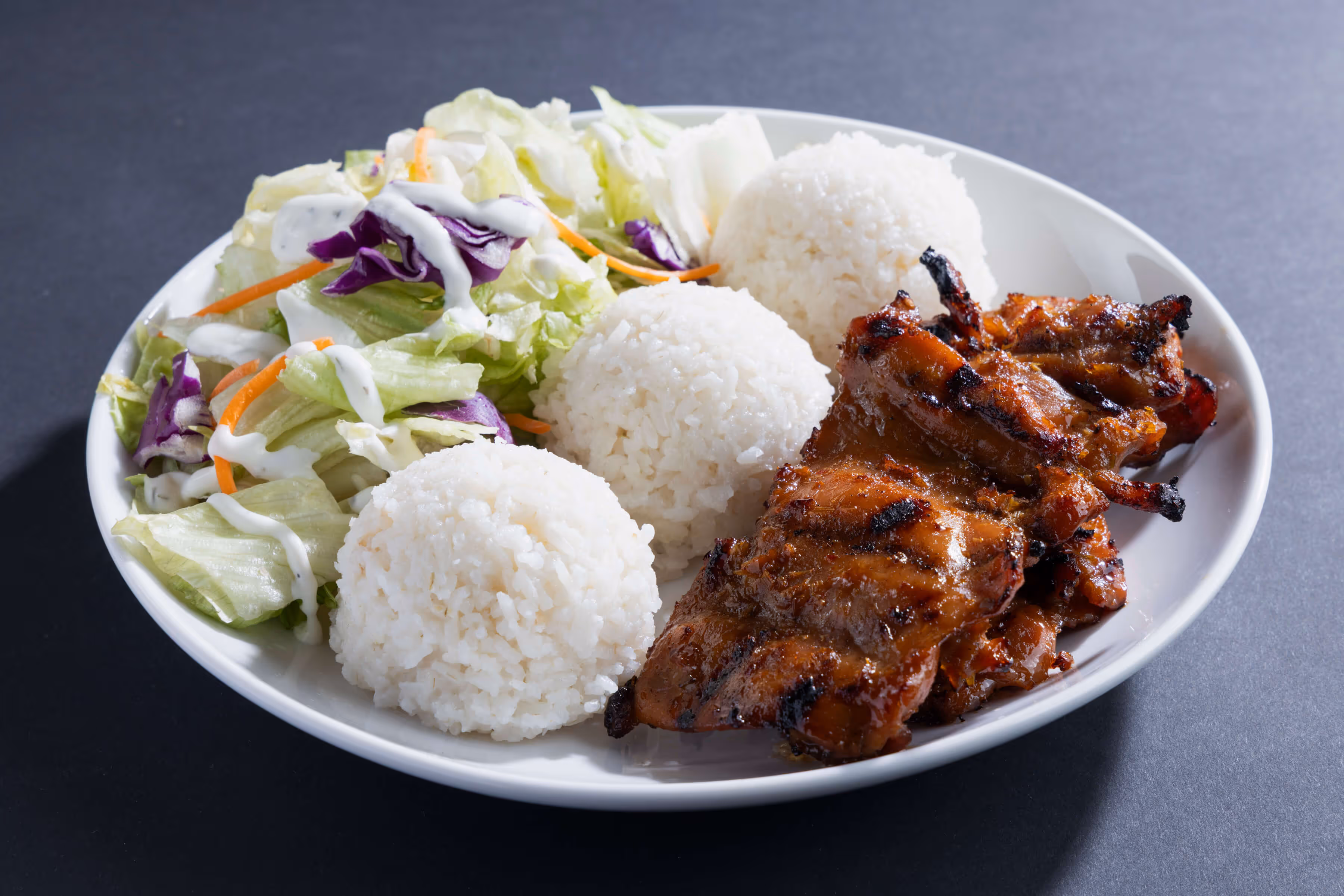Plate with grilled BBQ chicken, three scoops of white rice, and a side salad with lettuce, purple cabbage, carrots, and ranch dressing.