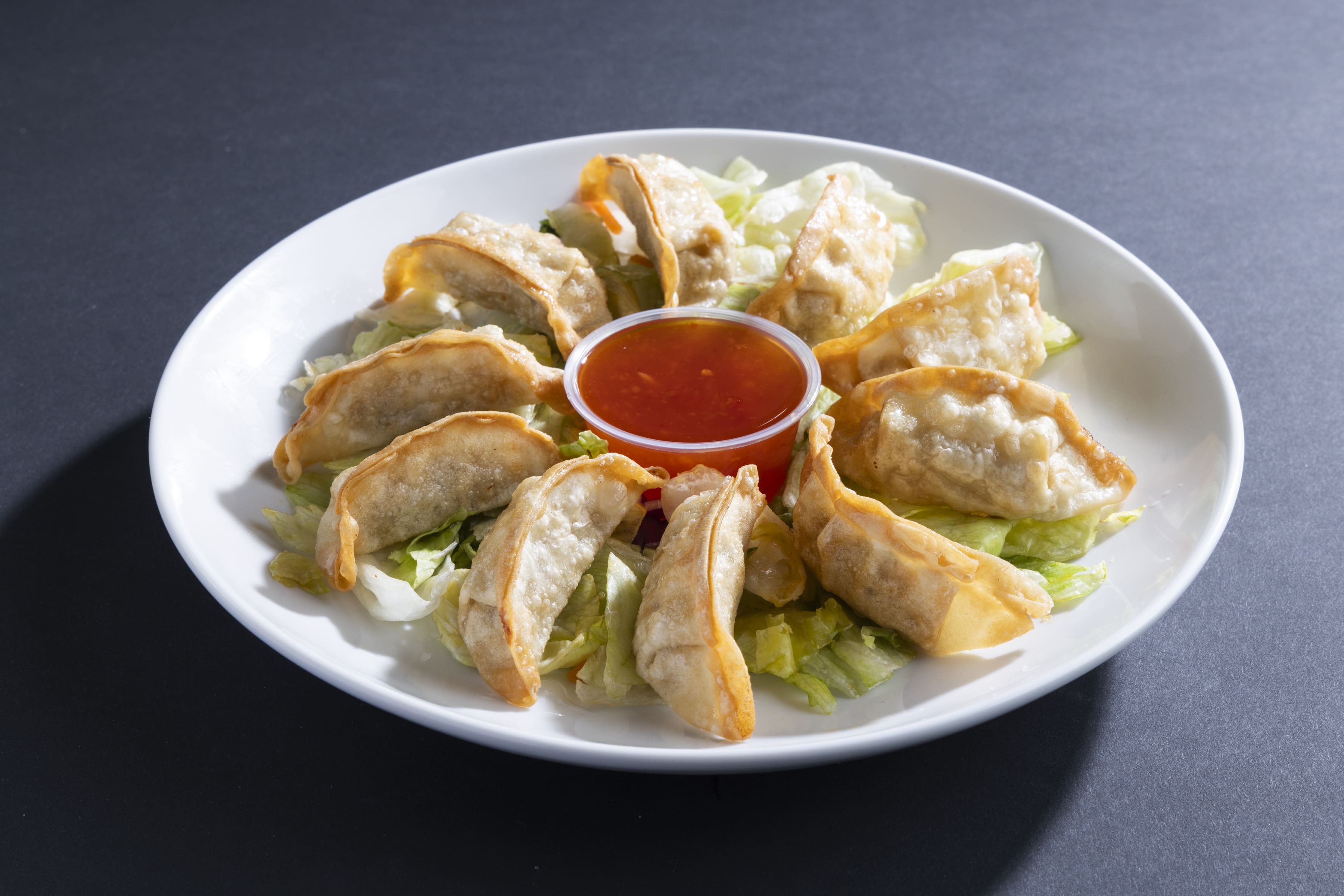 Plate of fried gyoza arranged in a circle on shredded lettuce with a cup of red dipping sauce in the center.
