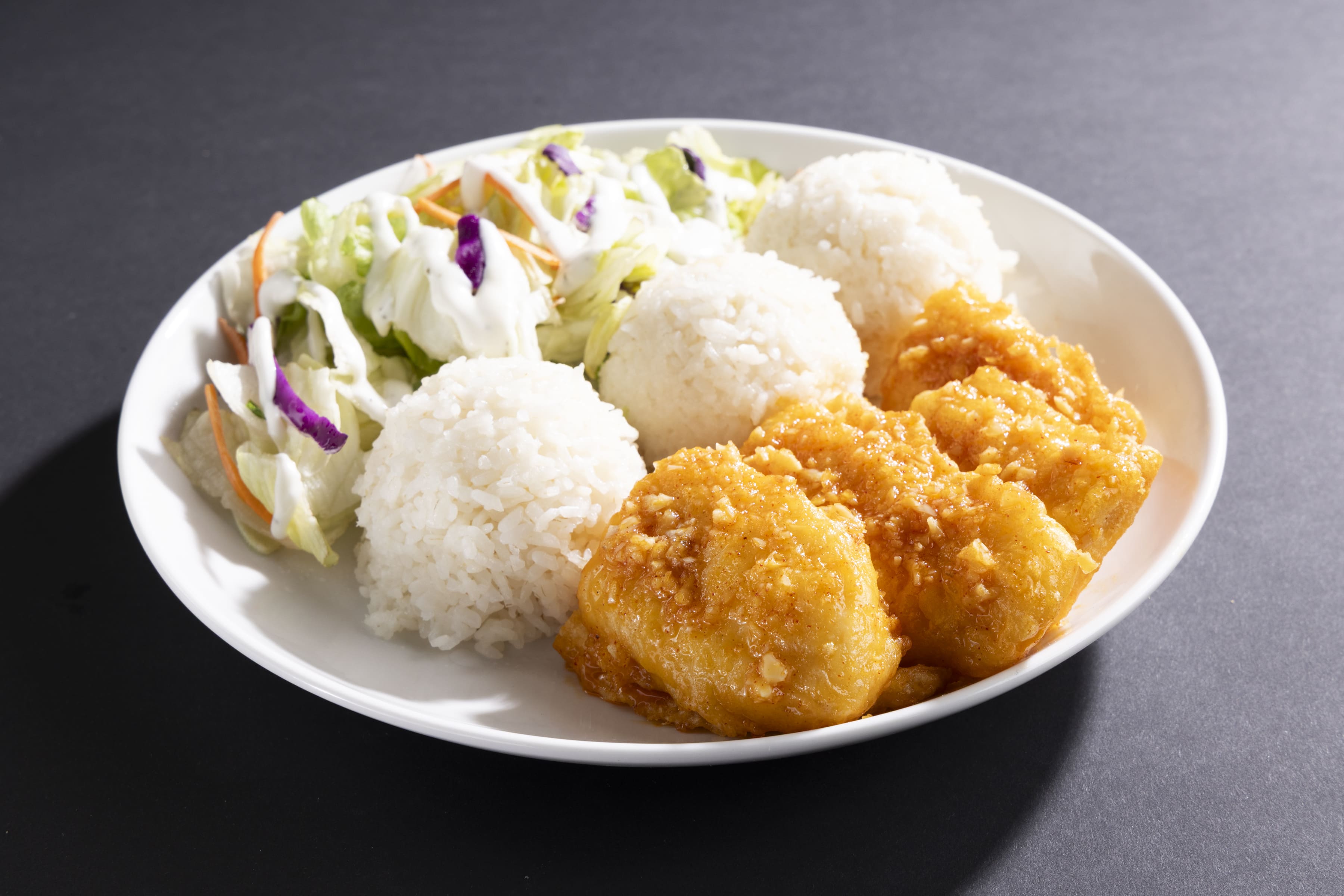 Plate with three scoops of white rice, fried garlic butter fish fillets, and a side salad with dressing.