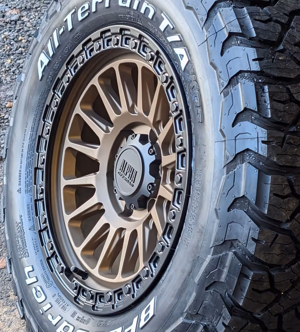 Close-up of an off-road BFGoodrich All-Terrain T/A tire mounted on a bronze Alpha Offroad wheel with rugged tread.
