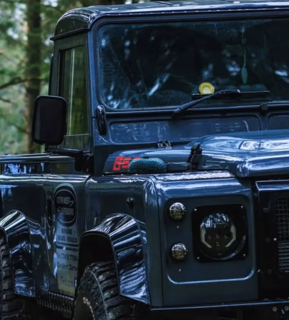 Front side view of a dark blue off-road vehicle with rugged tires parked in a forest.