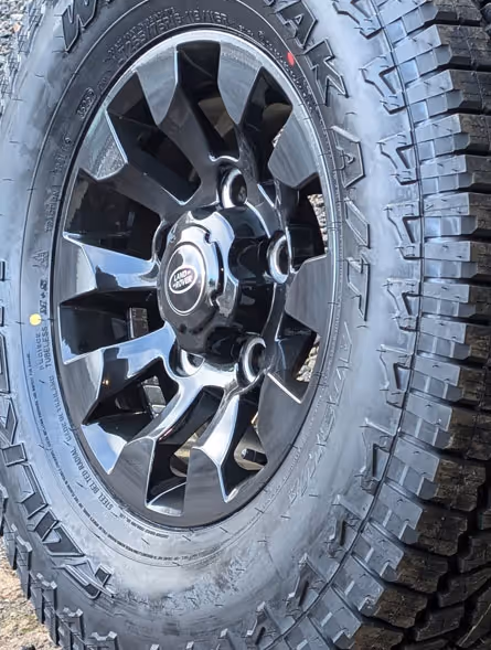 Close-up of a black Land Rover alloy wheel with an all-terrain tire mounted on it.