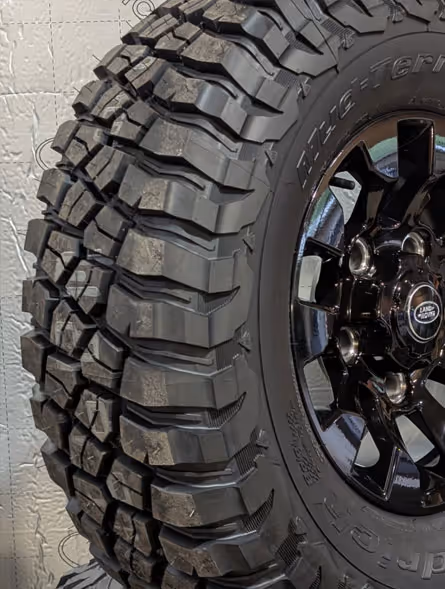 Close-up of a rugged off-road tire with deep treads mounted on a black Land Rover alloy wheel.