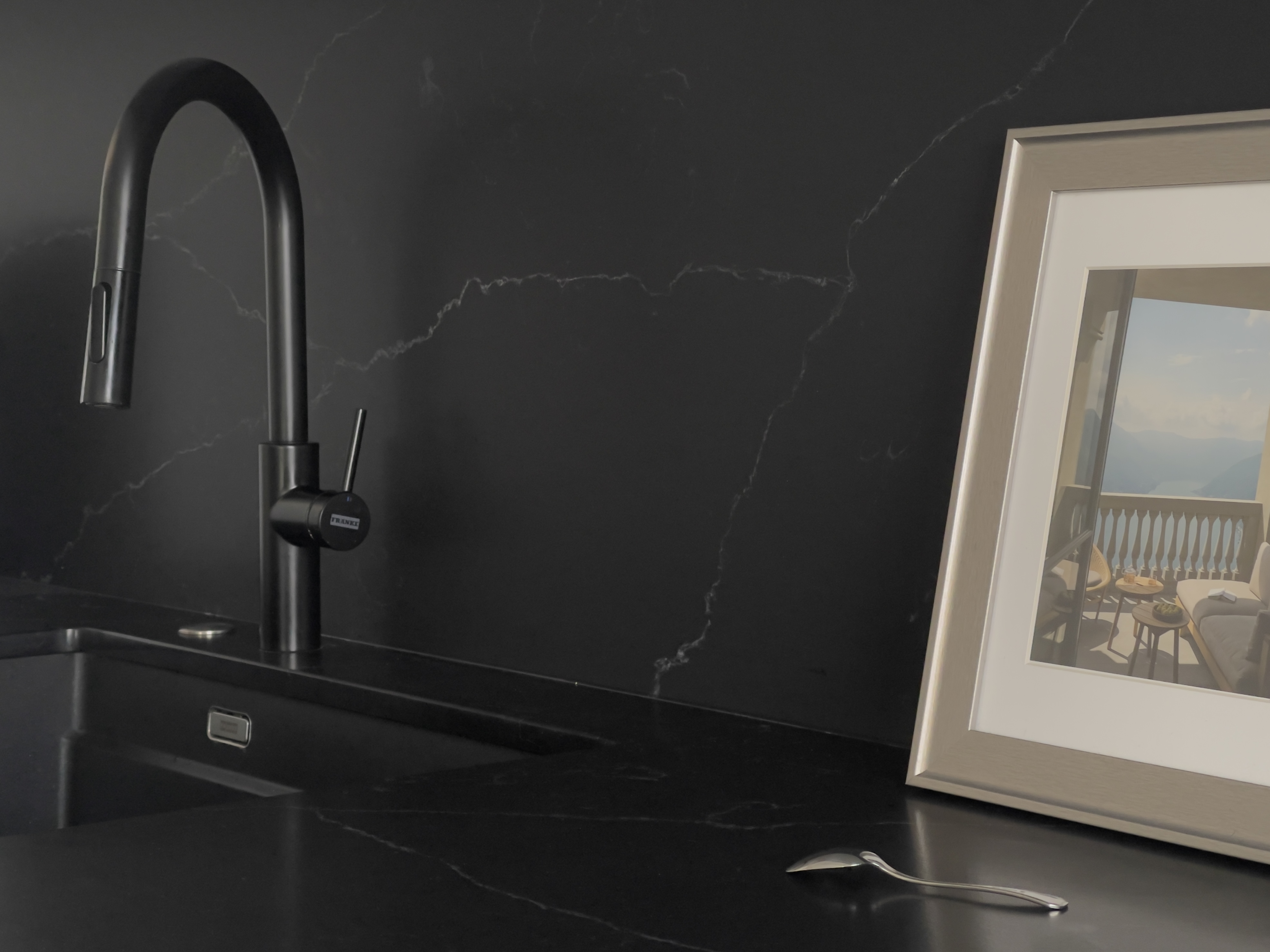 Czarna bateria i zlewozmywak podwieszany firmy Franke w białej kuchni z blatem z czarnego spieku.