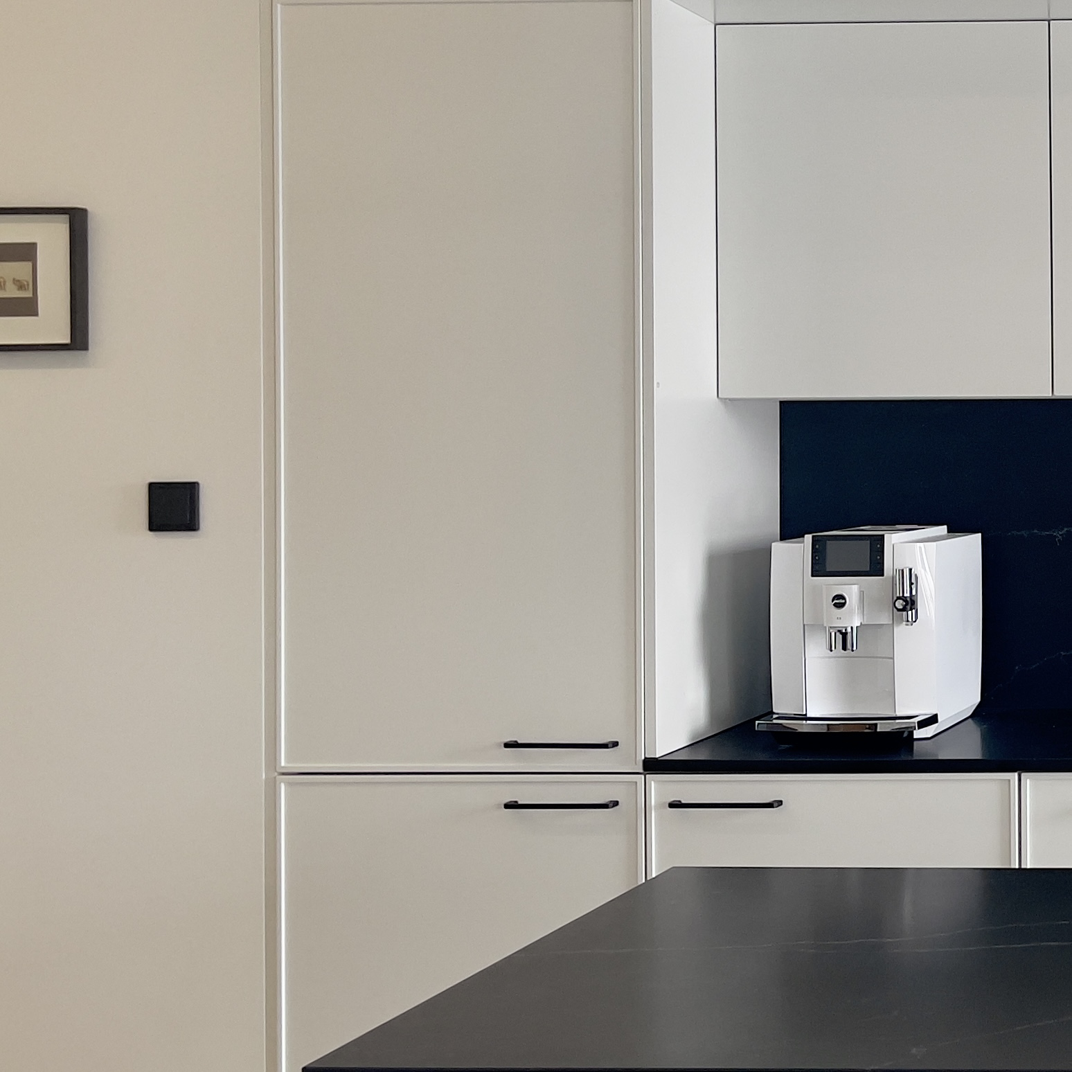 Ekspres do kawy i lodówka w zabudowie w białej kuchni z wyspą.