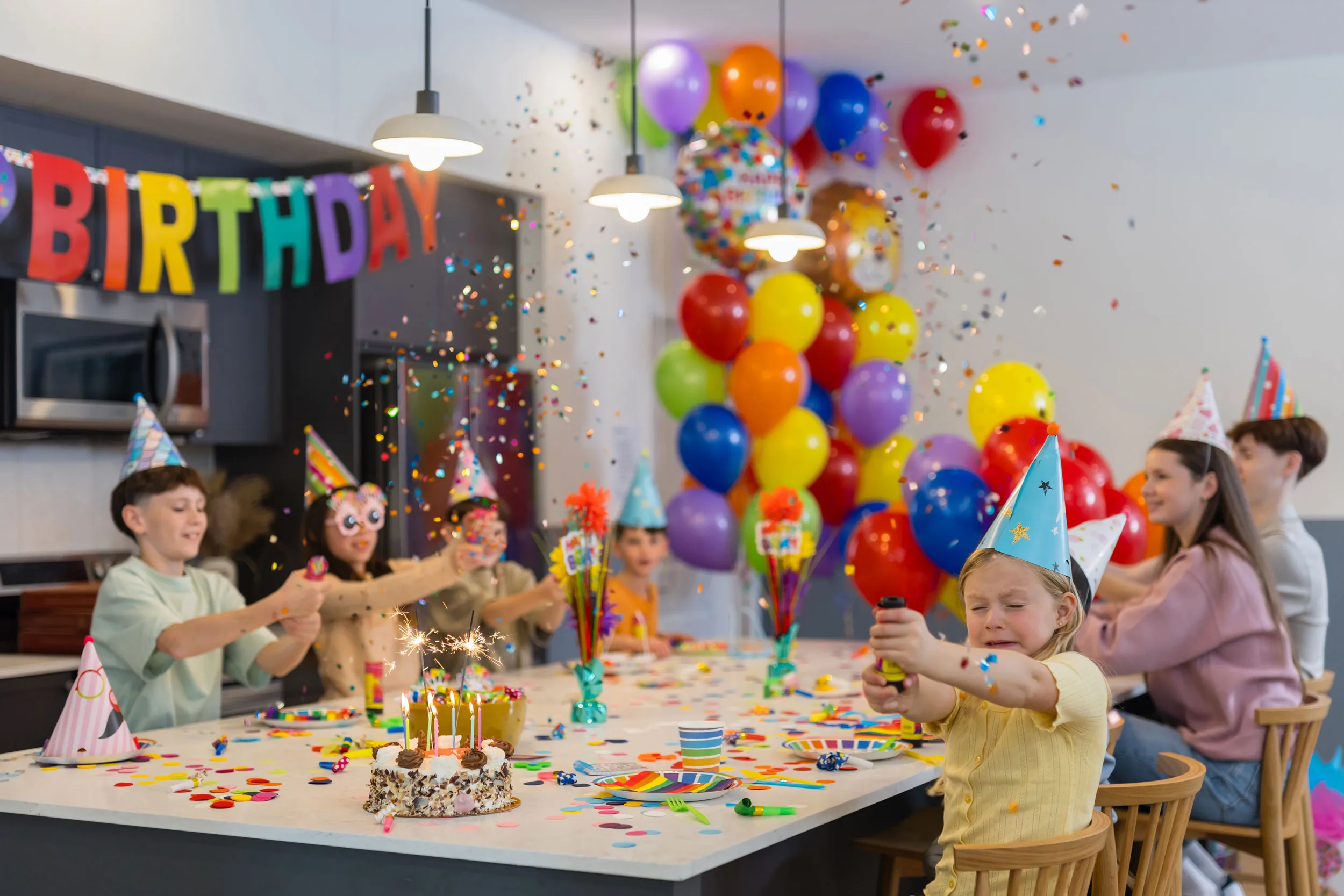 Children wearing party hats celebrate a birthday with confetti and sparklers around a cake on a decorated table at Queens in bear creek surrey