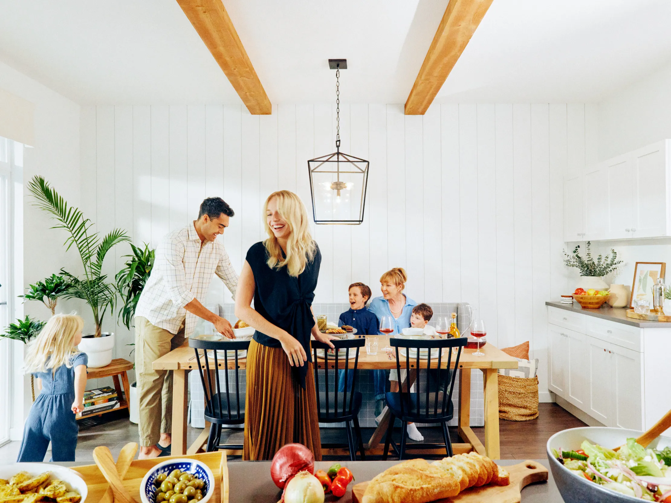 A family gathered in a bright dining room with wooden beams, enjoying a meal together and laughing at Fleetwood Village