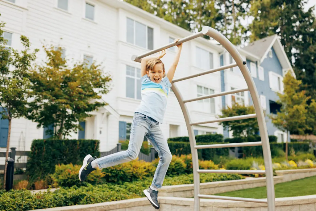 Young boy happily hanging and swinging on a curved metal jungle gym in a residential neighborhood playground at Fleetwood Village