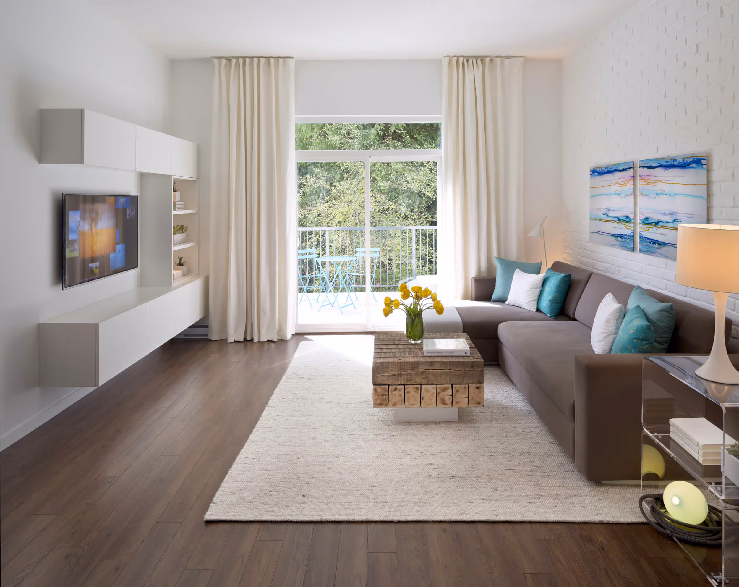 Modern living room with brown sectional sofa, turquoise cushions, wooden coffee table with yellow flowers, wall-mounted TV, On The Course townhomes