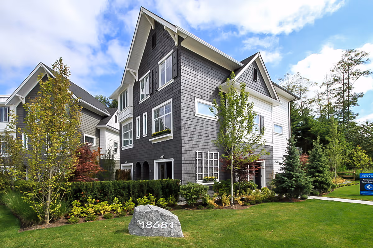 Modern two-story townhome with gray and white siding surrounded by green lawn and trees under a partly cloudy sky. Creekside by Dawson + Sawyer