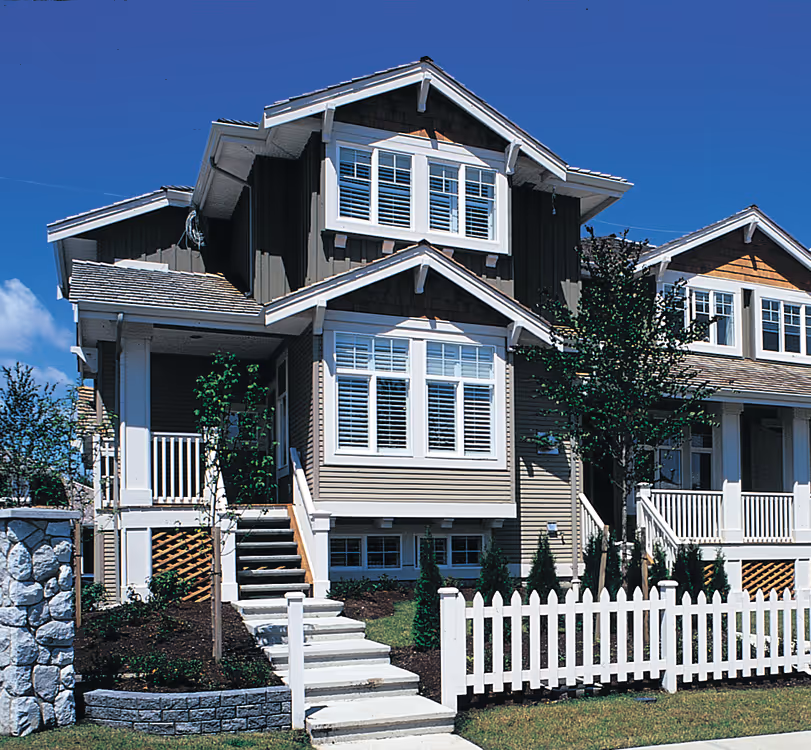 Two-story house with beige siding, white window shutters, a white picket fence, and a front porch under a clear blue sky. Redmill by Dawson + Sawyer