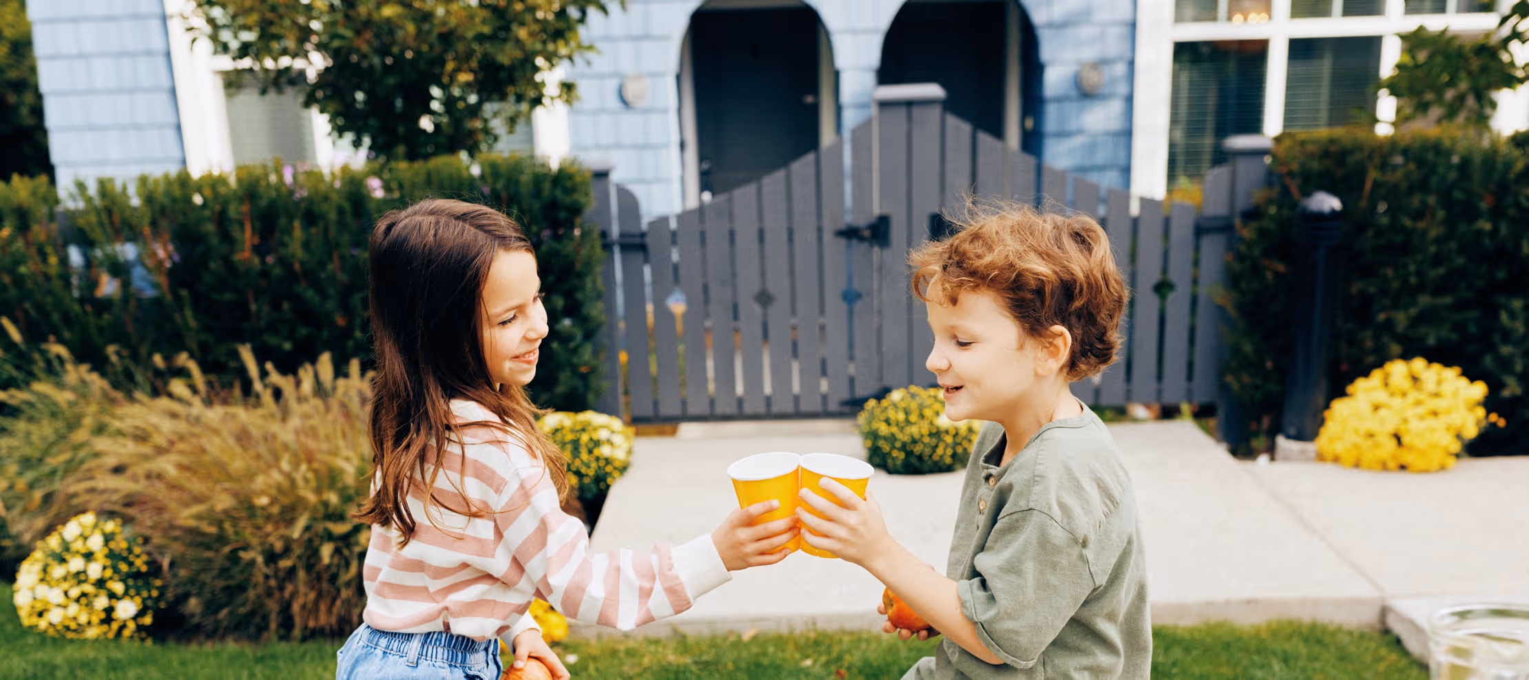 Two children smiling and clinking yellow cups in the garden of a Dawson + Sawyer townhome community