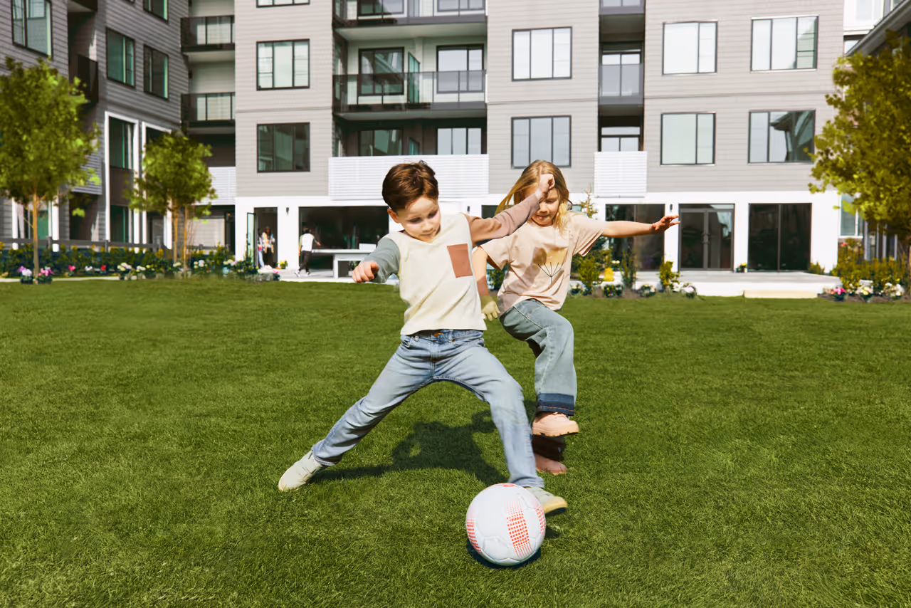 Children playing soccer on a grassy field at Bear Creek, part of the Queens Surrey community project, enjoying outdoor activity on a sunny day.