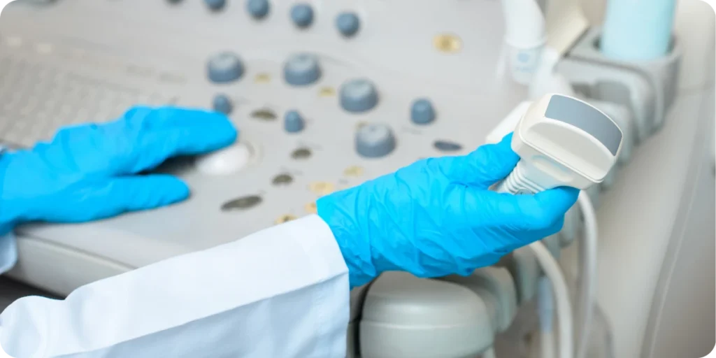 Close-up of a laboratory professional’s gloved hands operating an ultrasound probe connected to a medical imaging console, with control knobs and interface visible. The scene represents clinical diagnostics, medical device use, and regulated healthcare technology environments relevant to product compliance, device registration, and market access in China and the Asia-Pacific regulatory landscape.