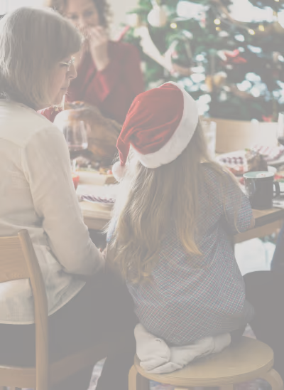 Une grand-mère et une petite fille portant un bonnet de Noël sont assises autour d'une table de fête décorée avec un sapin en arrière-plan.