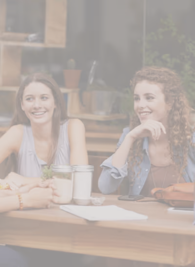Deux jeunes femmes souriantes assises à une table en bois discutant dans un cadre intérieur décontracté.