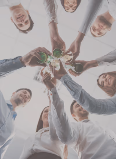 Un groupe de jeunes professionnels souriants trinquant avec des verres, vus d'en bas en cercle.