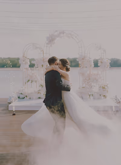 Un couple de mariés en train de s'embrasser et de danser lors d'une cérémonie de mariage en plein air au bord d'un lac.