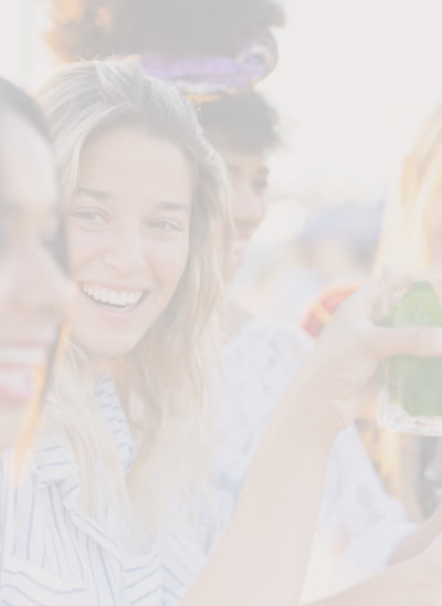 Groupe de jeunes femmes souriantes tenant un verre avec une boisson verte à l'extérieur.
