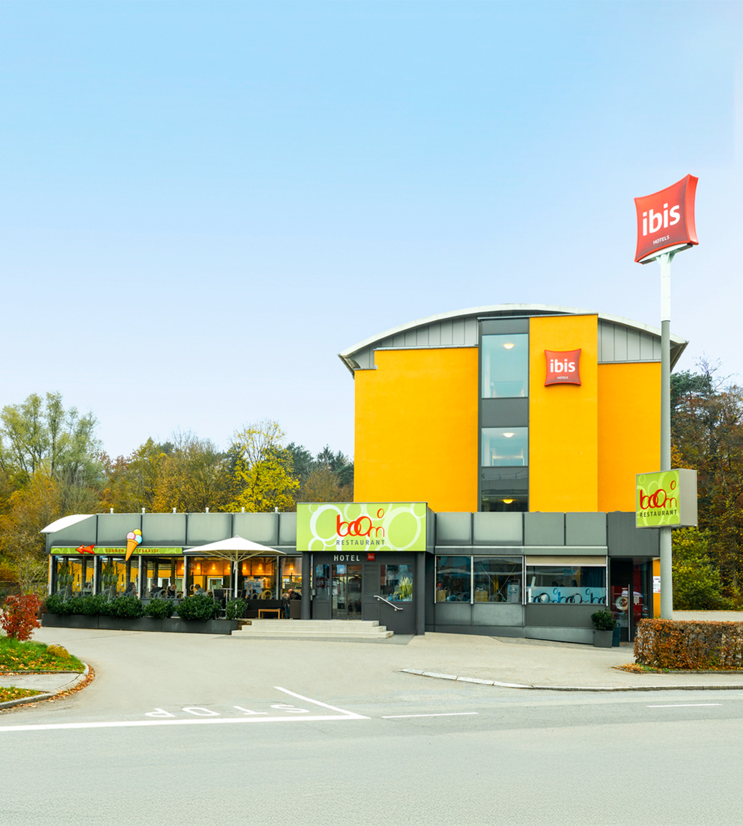 Leuchtend gelbes ibis Hotel in Adliswil mit Boom Restaurant und Außenbestuhlung an einem sonnigen Tag.