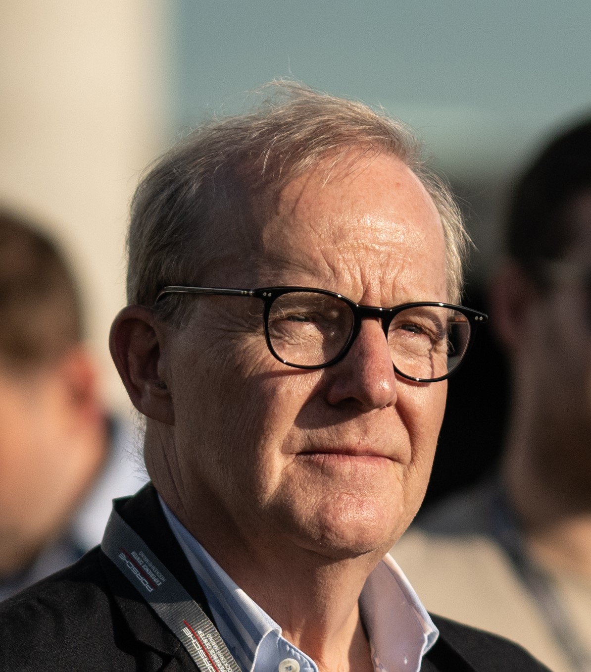 Porträt von Martin Studer, Inhaber von SHM, mit Brille im Sonnenlicht, unscharfe Personen im Hintergrund.