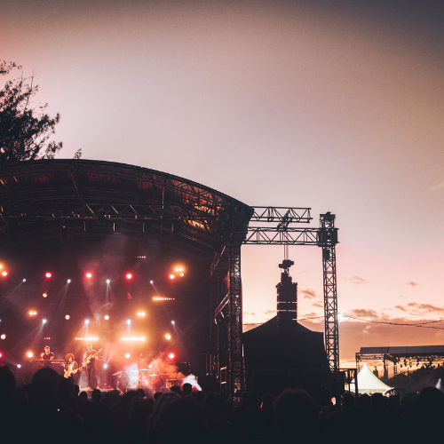 Scène de concert en plein air au coucher du soleil avec un groupe jouant devant une foule.