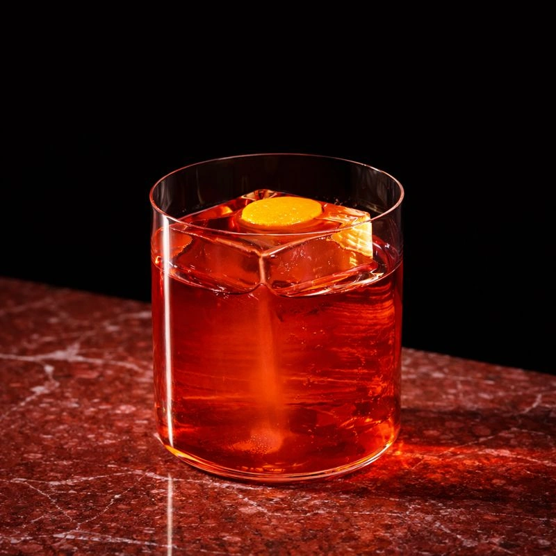 Cocktail à base de gin, d'amer italien et de vermouth rouge sur fond rose.