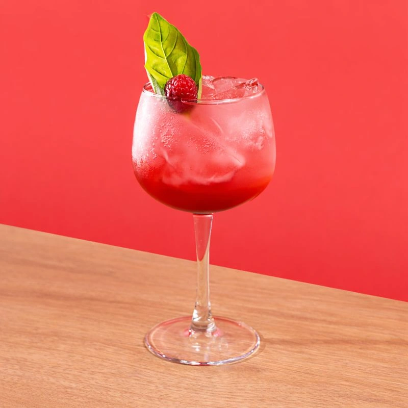 Cocktail made with Italian aperitif, raspberry syrup and tonic water on a red background.