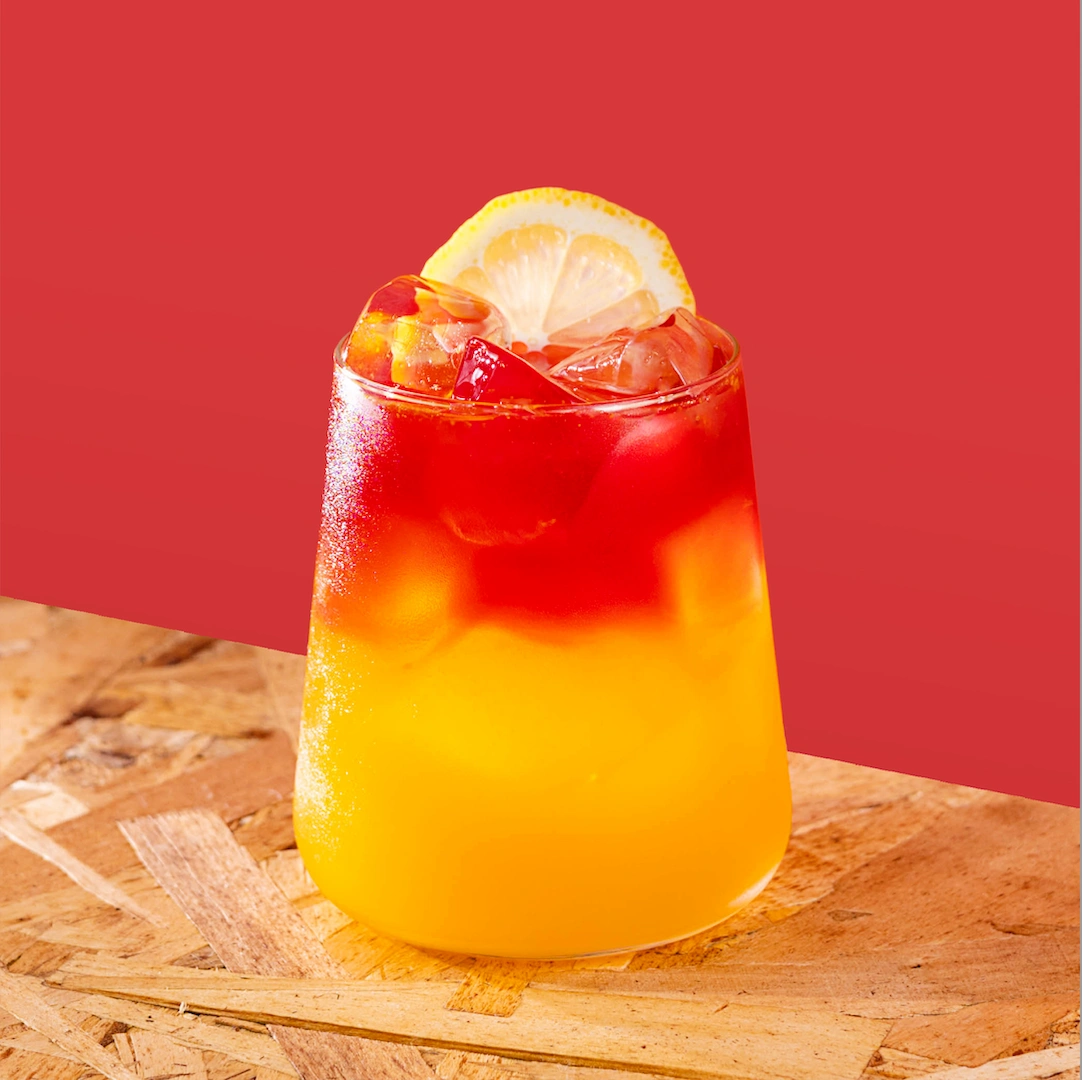 Cocktail à base de vodka, de sirop de pêche, de jus d'orange frais et de jus de canneberge sur un fond rouge.
