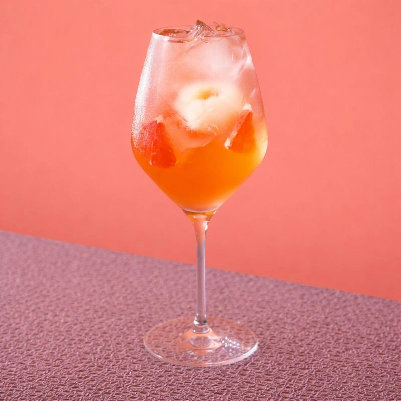 Cocktail à base de vin rosé, de sirop de litchi, de pamplemousse et d'eau pétillante sur fond rosé.