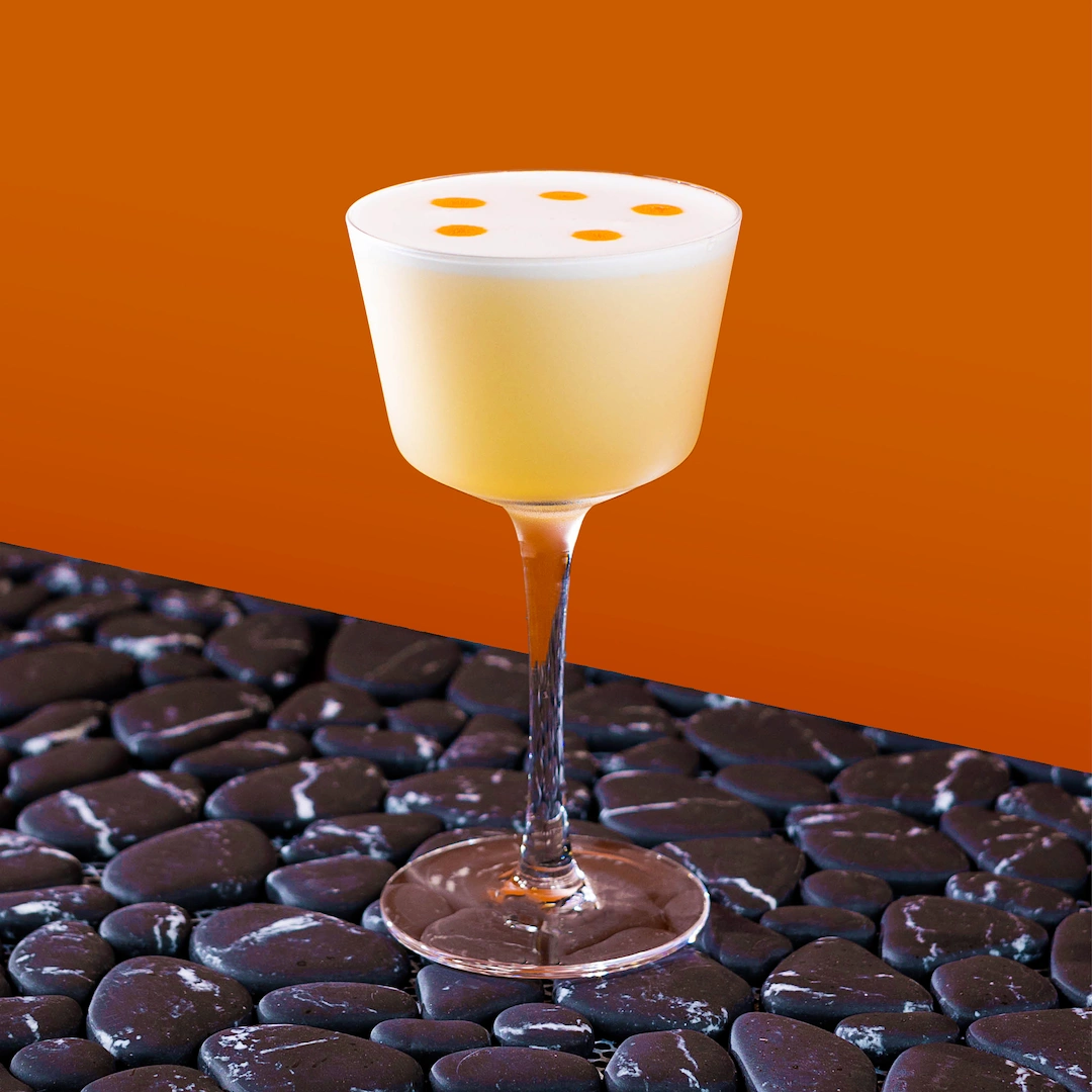 Cocktail made with spirits, lime syrup and egg white on a burnt orange background.