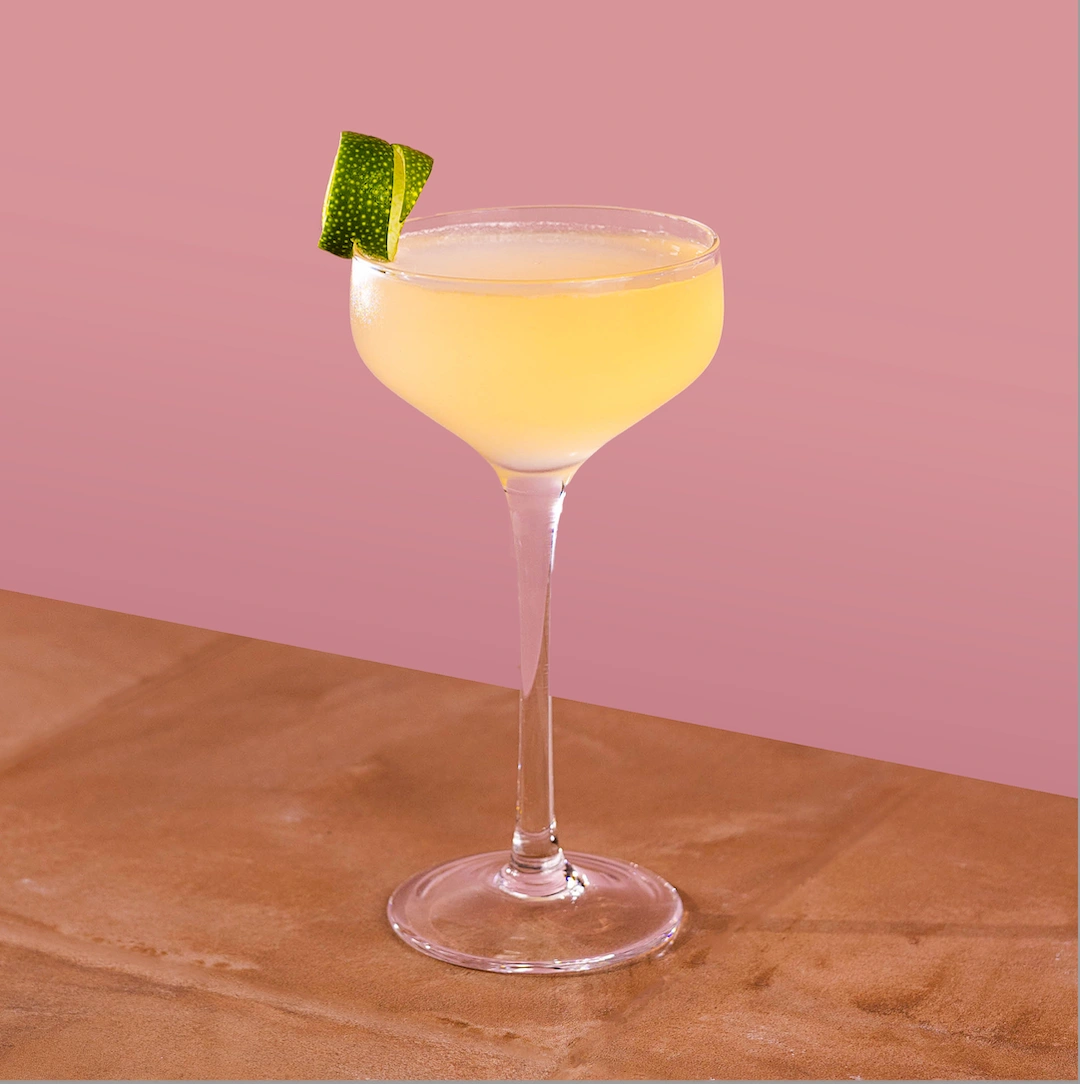 Cocktail made with gin and lime syrup on a rosé background.