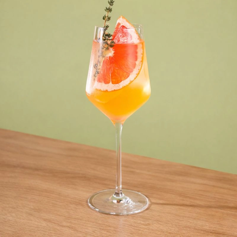 Cocktail à base de vin rosé, de gin, de sirop de licorne rouge, de mangue, de pamplemousse et d'eau pétillante sur fond vert.